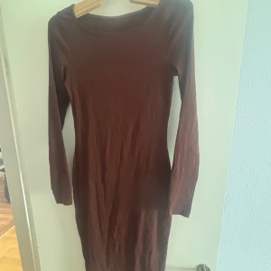 Brun långärmad klänning - En enkel och stilren brun klänning med lång ärm och rund halsringning. Modellen är kroppsnära och går ner till knäna, perfekt för dig som gillar en minimalistisk look. 