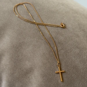 Guldhalsband med korsberlock - Snyggt halsband i 18k guld med en enkel korsberlock. Kedjan är tunn och smidig, perfekt för dig som gillar stilrena smycken. Låset är klassiskt och lätt att använda. Passar perfekt till dig som vill ha en tidlös detalj i din look.