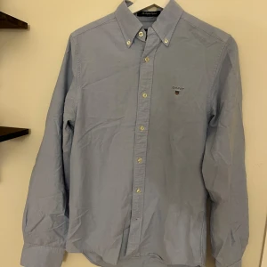 Ljusblå skjorta från Gant - Klassisk ljusblå skjorta från Gant med broderad logga på bröstet. Skjortan har button down-krage, långa ärmar och knäppning framtill. Perfekt för en clean och stilren look.