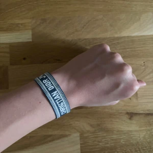 Christian Dior J'Adior armband blå - Snyggt armband från Christian Dior med texten 'J'Adior' i vitt på blå bakgrund. Armbandet är vävt i tyg och har fransar i ändarna för en cool touch. Perfekt accessoar för att lyfta din outfit med en exklusiv vibe.