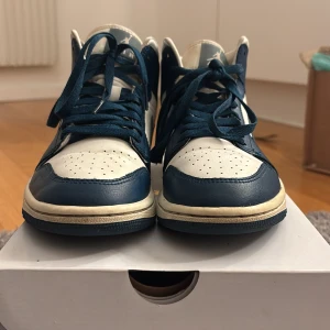 Nike Air Jordan 1 Mid blå/vit 38.5 - Nike Air Jordan 1 Mid i färgerna blå och vit med klassisk Jordan-logga på sidan. Skorna har snörning, rund tå och är tillverkade i skinn. Perfekt för dig som vill sticka ut med en ikonisk sneaker i snygg färgkombination.