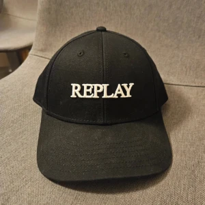 Svart keps från Replay - Snygg svart keps från Replay med vit broderad logga framtill. Klassisk böjd skärm och justerbar passform. Tillverkad i bomull för en bekväm känsla och stilren look. Perfekt accessoar för att lyfta din outfit.