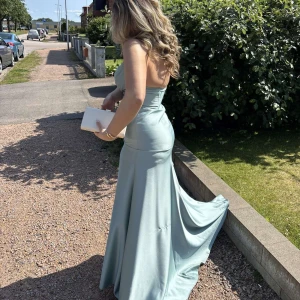 Ljusblå långklänning 🩵 - Superfin ljusblå långklänning med axelbandslös design och figurnära passform. Klänningen har en elegant släp, draperad överdel och är i satin material. Perfekt för bal eller student! Säljes då jag inte längre behöver den.