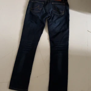 Mörkblå jeans från LTB - Snygga mörkblå jeans från LTB med klassisk femficksdesign och guldiga detaljer vid knappar och nitar. Jeansen har en smal passform och subtila slitningar framtill för en cool look. Perfekta till sneakers eller boots.