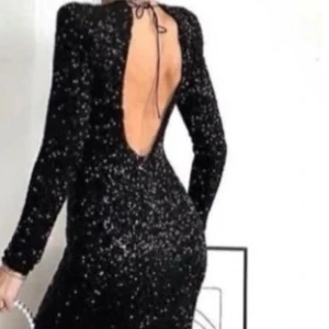 Zara långklänning med öppen rygg - Supersnygg svart lång-aftonklänning med glittriga paljetter och figurnära passform. Klänningen har långa ärmar och en djup öppen rygg som knyts i nacken. 