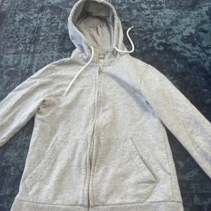 Grå hoodie med dragkedja från Etirel - Säljer en ljusgrå hoodie från Etirel i storlek XS. Tröjan har dragkedja framtill, huva med snörning och två stora fickor. Tillverkad i mjuk bomullsblandning, perfekt för chill dagar eller när du vill vara extra bekväm.