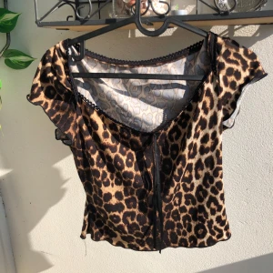 Leopardmönstrad topp - Snygg topp med leopardmönster i bruna och svarta toner. Modellen har korta volangärmar och en liten spetskant vid halsringningen, och två små svarta trådar i siden som man kan knuta rosett på (om du zoomar in så ser du nog.