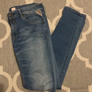 Replay Anbass ljusblå jeans herr - Snygga ljusblå Replay Anbass jeans med klassisk femficksdesign och gul kontrastsöm. Jeansen har en slim passform och är tillverkade i mjukt denimtyg. Märkets logga syns på fickan och bak på linningen. Perfekta för dig som gillar stilrena och bekväma jeans.