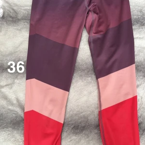 Färgglada leggings i rött och lila - Snygga leggings med breda blockränder i mörklila, rosa och rött. Tight passform och stretchigt material som passar perfekt till träning eller chill. Färgerna ger en cool och sportig vibe.🌸Små fläckar. Tvättlapp borta. Storlek 36 