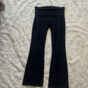 Svarta yoga pants Gina Tricot - Svarta yoga pants från Gina Tricot med bred, mjuk midja som kan vikas ner. Byxorna är i stretchigt material och har en skön passform med utsvängda ben. Perfekta för en chill och trendig look.