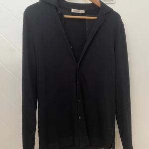 Mörkblå merinoullscardigan från Suitsupply - Stilren mörkblå cardigan från Suitsupply i mjuk merinoull. Klassisk krage, långärmad och med knappar framtill. Perfekt för dig som gillar en clean och tidlös look. Cardiganen är tunn och följsam, vilket gör den riktigt skön att bära.