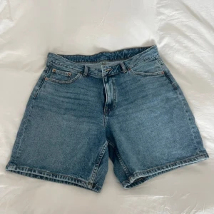 Blåa jeansshorts från Dr Denim - Snygga blåa jeansshorts från Dr Denim i klassisk modell med fem fickor och bälteshällor. De är högmidjade och har en rak, loose passform som slutar ovanför knäna. Perfekta för sommaren och lätta att matcha med allt. Materialet är 100% bomull för en skön känsla.