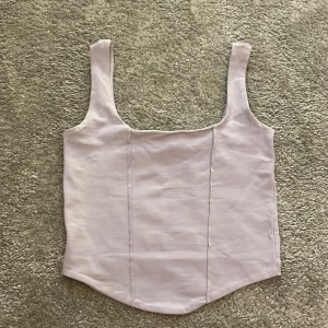 Ljuslila linnetopp från Gina Tricot - Supersöt ljuslila linnetopp från Gina Tricot med breda axelband och lätt figursydd passform. Toppen har en enkel, stilren design med markerade sömmar framtill och en något rundad nederkant. Perfekt att matcha med jeans eller kjol för en fräsch look. Köp gärna!