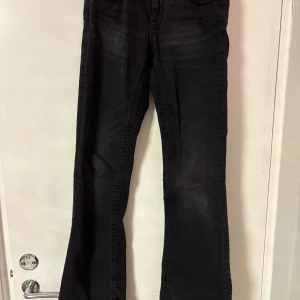 Svarta bootcut jeans från Ginatricot - Svarta jeans från Ginatricot i bootcut-modell med klassiska fem fickor och snygga silverfärgade knappar. Jeansen har en lätt utsvängd passform nertill och är gjorda i mjukt denimtyg. Perfekta för dig som gillar en tidlös look med lite edge.