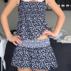 Blommig set med smock - Supersött sett med smala axelband och smockad överdel. Settet är marinblått med små vita blommor över hela tyget och har en luftig kjol. Perfekt för varma dagar och ger en fräsch sommarkänsla. Aldrig använt! Helt nytt skick!🥰Topp i xs kjol i s🌸