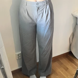 Gråa vida kostymbyxor - Snygga grå kostymbyxor med hög midja och vida ben. Byxorna har pressveck framtill, knäppning med knapp och dragkedja samt fickor i sidorna💕💕