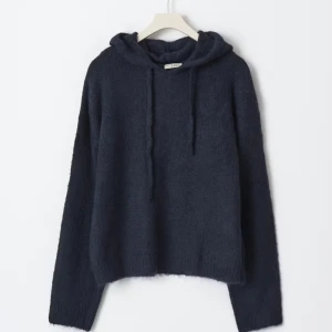 Mörkblå stickad hoodie med huva - Mysig mörkblå stickad hoodie från Gina tricot med huva och snörning. Tröjan har en loose passform och långa ärmar, perfekt för kyliga dagar. Materialet är mjukt och fluffigt, vilket ger en avslappnad och trendig look.