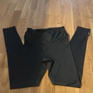 Svarta tights från 157 i storlek S - Svarta tights från 157 i stretchigt syntetmaterial. De har en tight passform och hög midja, perfekta för träning eller chill. Stilren design utan synliga detaljer förutom en liten logga vid höften.