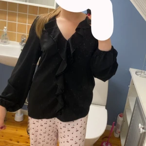 Svart blus med volanger  - Säljer en svart blus med volanger, storlek L, knappt använd, säljer den för 50kr + frakt!
