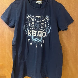 Mörkblå Kenzo t-shirt med tigertryck - Snygg mörkblå t-shirt från Kenzo med ikoniskt tigertryck och logga på bröstet. Klassisk rund halsringning och korta ärmar. Tillverkad i mjuk bomull som känns skön mot huden. Perfekt för dig som vill sticka ut med en cool streetstyle-look.