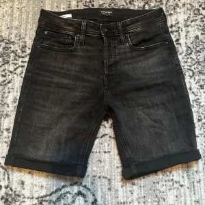 Svarta jeansshorts från Jack & Jones - Svarta jeansshorts från Jack & Jones i klassisk femficksmodell. Shortsen har upprullade benslut, normal passform och midja, samt diskreta slitningar för en cool look. Perfekta för dig som gillar en enkel och stilren vibe.