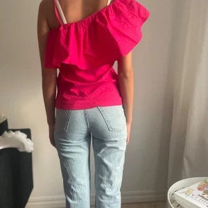 Rosa offshoulder topp från Ellos - Säljer en snygg rosa offshoulder topp från Ellos i storlek 34/36. Toppen har en stor volang över bysten och ena axeln är bar för en cool look. Perfekt för dig som vill sticka ut med färg och form. Materialet känns lätt och skönt mot huden.