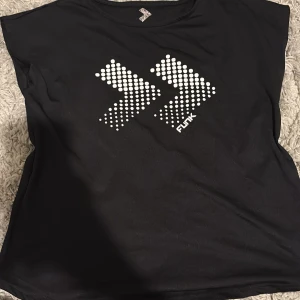 Svart topp från 157 Funk med tryck - Svart ärmlös topp från 157 Funk med coolt vitt grafiskt tryck framtill i form av två pilar av prickar. T-shirten har rund halsringning och är gjord i mjuk bomull, perfekt för en sportig och avslappnad stil.