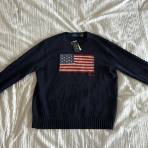 Mörkblå stickad tröja Polo Ralph Lauren - Polo Ralph Lauren tröja – helt ny med tag! Mörkblå, stickad med broderad amerikansk flagga och RL-detalj. Storlek Medium. Nypris runt 5000 kr – din för mindre!