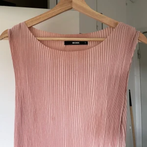 Plisserad rosa långklänning Bik Bok - Supersnygg plisserad långklänning från Bik Bok i en mjuk rosa nyans. Klänningen är ärmlös med rund halsringning och har en rak, flowy passform. Perfekt för dig som gillar stilrena och trendiga plagg med lite extra struktur.