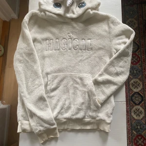 Vit fluffig hoodie med enhörningsdetaljer - Supermjuk och fluffig vit hoodie från H&M med broderad text 'MAGICAL' på bröstet. Huvan har söta enhörningsdetaljer som horn, öron och broderade ögon.  