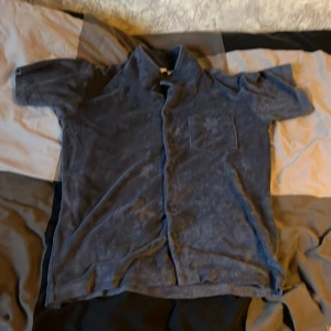 Blå frottéskjorta med kort ärm - Mjuk och chill blå skjorta i frotté med korta ärmar och knappar hela vägen. Bröstficka på vänster sida ger en avslappnad vibe. Perfekt för dig som gillar bekväma och lite annorlunda plagg.