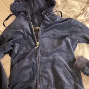 Mörkblå velourjacka Juicy Couture XS - Sitter mer som storlek ”S” än ”xs” Mörkblå kofta  från Juicy Couture med huva, dragkedja med guldfärgad J-detalj och broderad logga på bröstet. Jackan har känguruficka och ribbade muddar. Perfekt för en chill och trendig look.