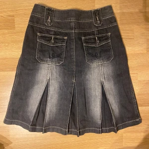 Jeanskjol - Cool svart jeanskjol med markerade sömmar, stora fickor fram och bak samt snygga slitsar nertill. Kjolen har en lätt utsvängd form och midjehög passning. Perfekt till boots och en croppad topp för en trendig look.