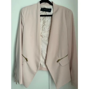 Elegant ljusrosa kavaj från ZARA BASIC – Strl M  - ✨ Elegant ljusrosa kavaj från ZARA BASIC – Strl M ✨  Säljer en superfin och stilren kavaj från ZARA BASIC i en vacker ljusrosa/beige ton – perfekt för både vardag och fest! Kavajen är i storlek M (EUR M, USA M, MEX 28) och har en öppen design utan knappar, vilket ger en avslappnat elegant look. Detaljer som guldfärgade dragkedjor vid fickorna och ärmsluten ger plagget en modern och lyxig känsla. Insidan är fodrad med ett satinliknande tyg i matchande ljusbeige färg.  