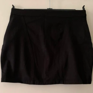 Svart kortkjol med dragkedjor H&M - Svart kortkjol från H&M i stilren modell med två sneda dragkedjor bak och en synlig dragkedja i mitten. Kjolen har en figurnära passform och är gjord i ett mjukt bomullstyg. Perfekt till sneakers eller boots för en cool look.