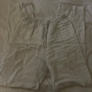 Vita linnebyxor med snörning - Luftiga och sköna linnebyxor i vitt med elastisk midja och dragsko. Byxorna har raka ben och en avslappnad passform, perfekta för varma dagar. Materialet är tunt och andas bra, vilket gör dem extra bekväma. Obs! Skav mellan benen på yttersta lagret, finns alltså två lager så inget som synts. 