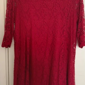Röd spetsklänning från Isolde - Röd klänning från Isolde med vackert blommigt spetsmönster och trekvartsärm. Klänningen är fodrad och har en rak, något lös passform. Perfekt för dig som vill sticka ut med en elegant och färgstark look.