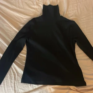 Svart ribbad polotröja från BikBok - Svart polotröja från BikBok i storlek L. Tröjan är ribbad och har lång ärm samt hög polokrage. Perfekt för lager-på-lager och funkar till många olika outfits. Materialet är mjukt och stretchigt för en skön passform.