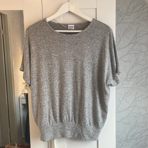 Gråmelerad stickad tröja Stories - Gråmelerad stickad tröja från Stories med avslappnad passform och korta ärmar. Tröjan har rund halsringning och bred mudd nertill för en snygg siluett. Perfekt för lager-på-lager och chill vibes.