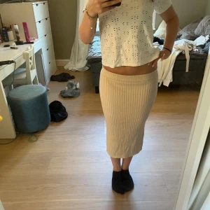 Beige ribbad stickad långkjol - Säljer en beige ribbad stickad långkjol med låg midja och rak passform. Kjolen är mjuk och stretchig, perfekt för en chill och snygg look. Passar lika bra med sneakers som boots. Enkel att matcha med olika toppar.