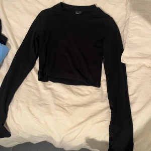 Svart croppad långärmad tröja - En svart, croppad långärmad tröja med enkel design och rund hals. Perfekt att matcha med höga jeans eller kjol för en clean look. Mjuk och stretchig bomullskänsla som sitter snyggt på kroppen.