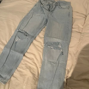 Ljusblå ripped jeans med raka ben - Säljer ett par ljusblå jeans med raka ben och snygga slitningar över båda knäna. Klassisk femficksmodell med normal passform och hög midja. Perfekta för en avslappnad streetstyle-look.