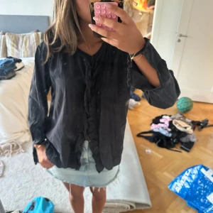 Svart blus med volangdetaljer❣️ - Svart blus med långa ärmar och snygga volangdetaljer längs knäppningen framtill. Skjortan har en lös passform och är tillverkad i ett lätt tyg som känns skönt mot huden. Hör gärna av er för fler bilder eller frågor!❣️❣️