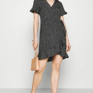 Svart vit prickig omlottklänning  - Supersöt svart klänning från Vero Moda med vita prickar, omlottmodell och volangdetaljer. Klänningen har korta ärmar och knyt i midjan för en snygg passform. Första två + sista två lånade!🥰