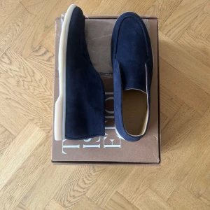 Mörkblå mocka loafers från Etiq - Stilrena loafers i mörkblå mocka från Etiql. Skorna har en klassisk rund tå, vit platt sula och är tillverkade i mjukt mockamaterial. Perfekta för dig som gillar en clean och modern look med en twist av premiumkänsla. Skorna är dessutom helt sprillans nya rakt ur lådan!