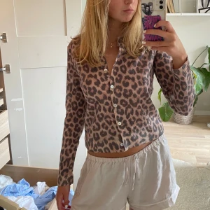 Leopardmönstrad kofta med knappar - Säljer en snygg leopardmönstrad kofta med långa ärmar och vita knappar framtill. Koftan är i beige och bruna toner, har en croppad passform och är tillverkad i ett mjukt stickat material. Perfekt för dig som vill sticka ut lite extra.