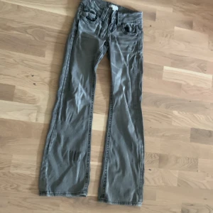 Grå bootcut jeans Gina Tricot 146 - Snygga grå jeans från Gina Tricot i storlek 146. Modellen har bootcut-ben och klassisk femficksdesign. Jeansen har två silverfärgade knappar framtill och är tillverkade i ett mjukt bomullsmaterial. Perfekta för dig som gillar en avslappnad men trendig look.