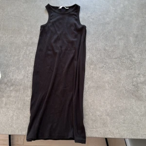 Svart ribbad klänning från H&M - En svart, ärmlös ribbad klänning från H&M i stretchigt material. Modellen är enkel och skön  med rund halsringning och rak passform, perfekt för en clean och stilren look. Klänningen är en kortklänning och passar dig som gillar minimalistisk stil. Perfekt till dig som drar till stranden och bara vill ha något över.