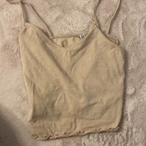 Beige linnetopp från H&M Divided XXS - Säljer en enkel och stilren beige linnetopp från H&M Divided i storlek XXS. Toppen har smala axelband och en rak passform. Materialet är mjukt och skönt, perfekt för varma dagar. Nedtill finns en liten vågig detalj som ger toppen en söt touch.