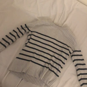 Randig ribbstickad tröja från H&M - Säljer en ribbstickad tröja från H&M i beige med svarta horisontella ränder. Tröjan har lång ärm och en klassisk rund halsringning. Perfekt för dig som gillar en enkel men stilren look.